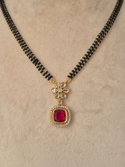 Prisham Mangalsutra close-up view of gold floral pendant with red CZ stone and black bead chain by Naitri