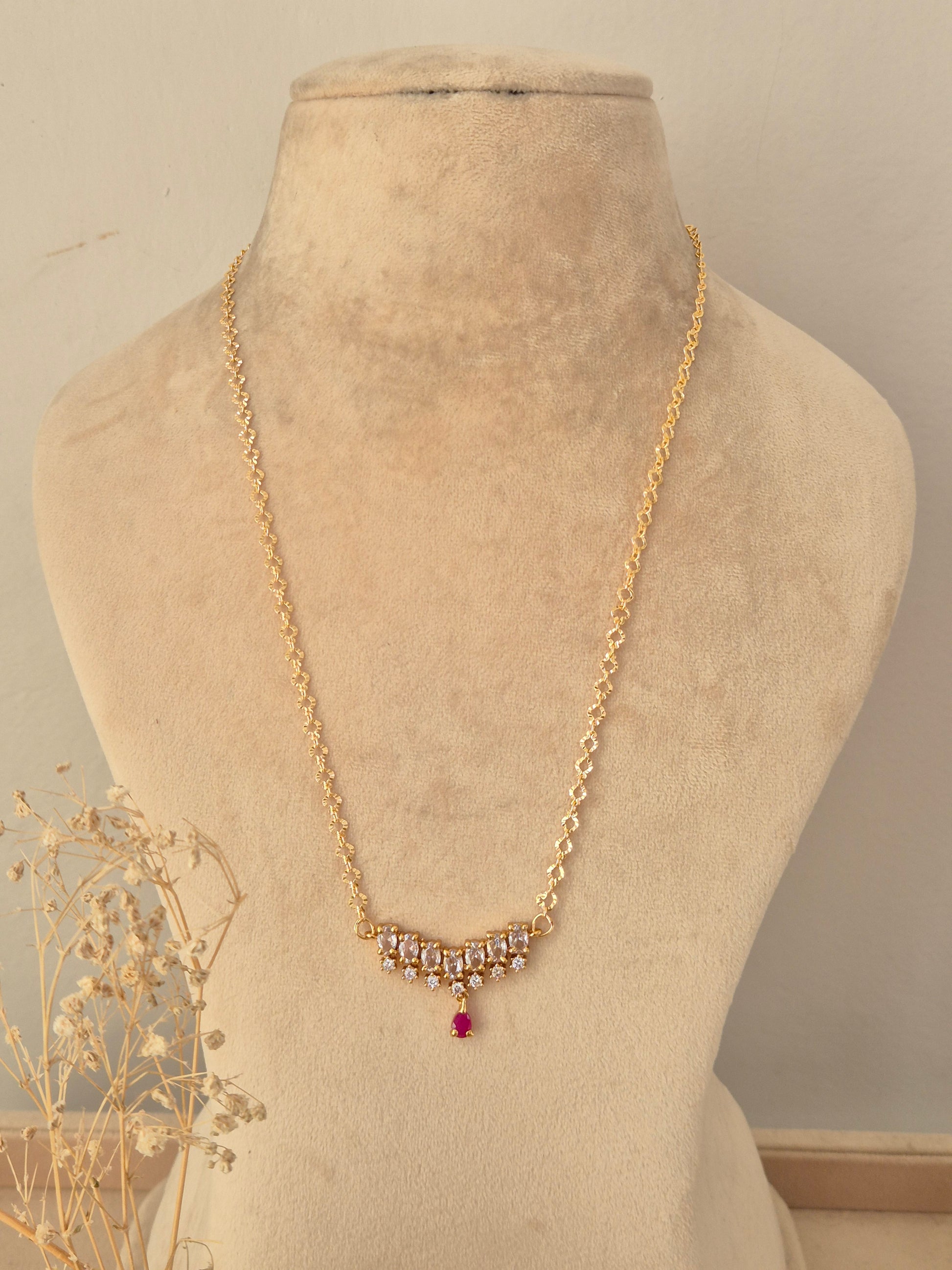 Zaahra Necklace featuring a gold chain with clear CZ stone clusters and a ruby-pink teardrop pendant drop