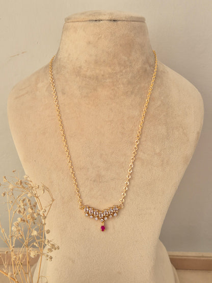 Zaahra Necklace featuring a gold chain with clear CZ stone clusters and a ruby-pink teardrop pendant drop