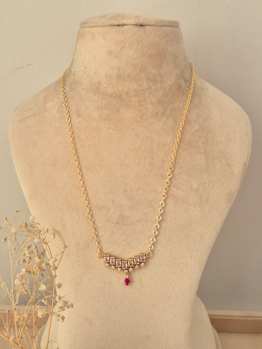 Zaahra Necklace featuring a gold chain with clear CZ stone clusters and a ruby-pink teardrop pendant drop