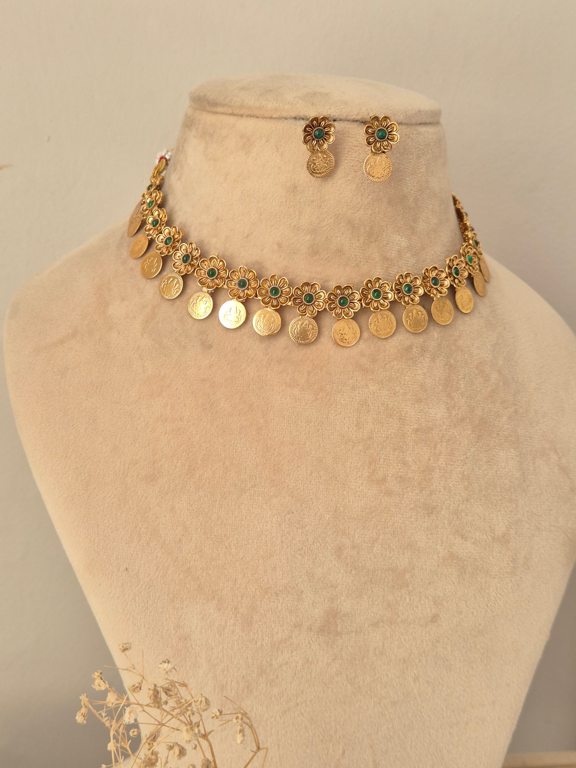 Zoyna Necklace Set showcasing an antique gold-toned choker adorned with floral motifs centered with emerald-green stones and dangling coin charms, displayed on a beige mannequin bust with matching round drop earrings