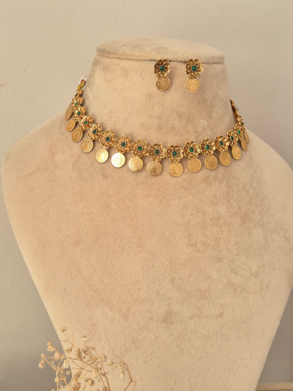 Zoyna Necklace Set showcasing an antique gold-toned choker adorned with floral motifs centered with emerald-green stones and dangling coin charms, displayed on a beige mannequin bust with matching round drop earrings