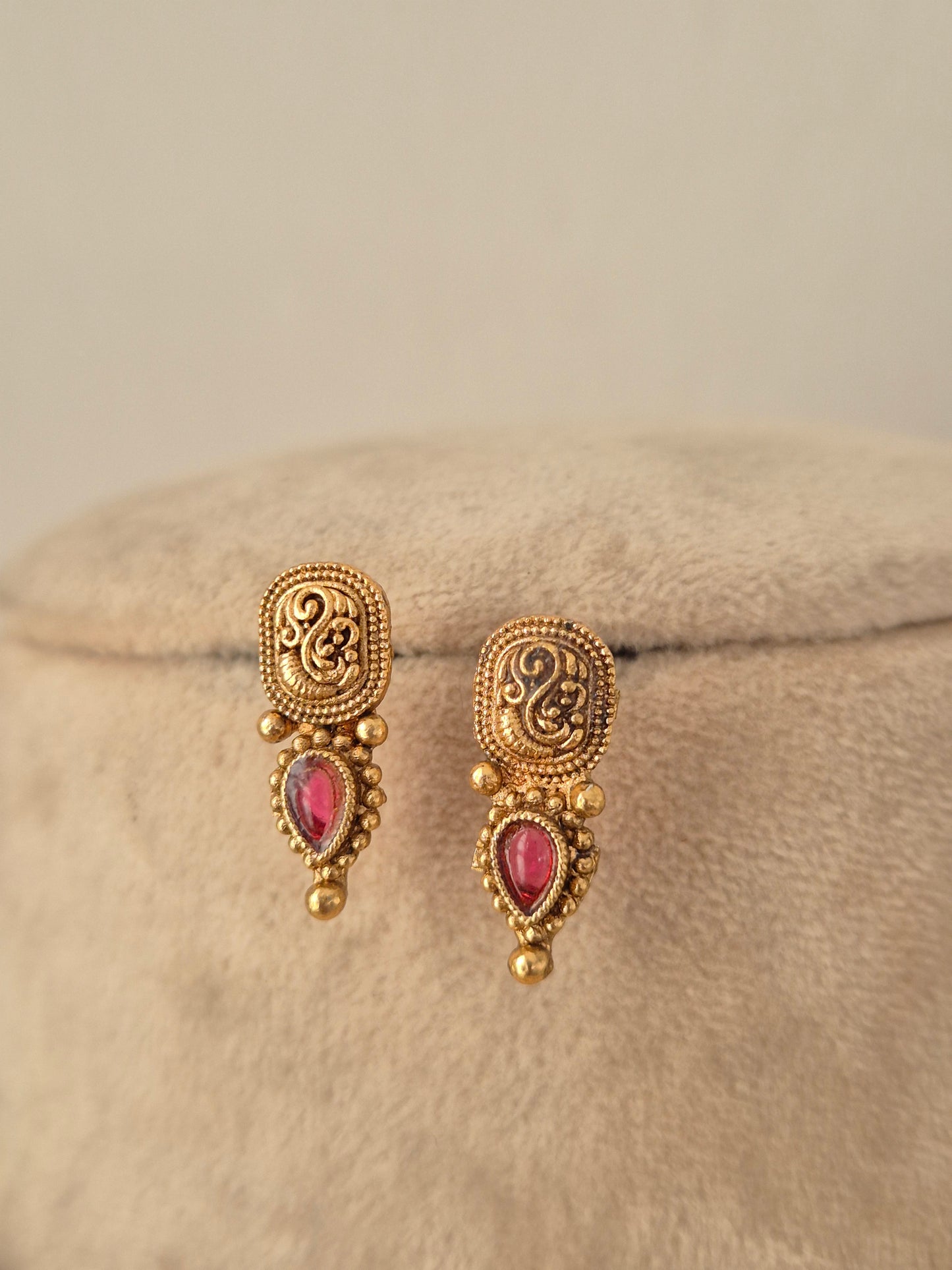 Close-up view of antique gold drop earrings set with pear-shaped ruby-pink stones and intricate peacock motifs