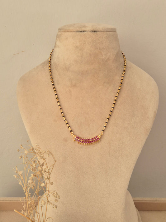 Antique gold mangalsutra featuring a traditional pendant with ruby-pink drop stones, black bead chain