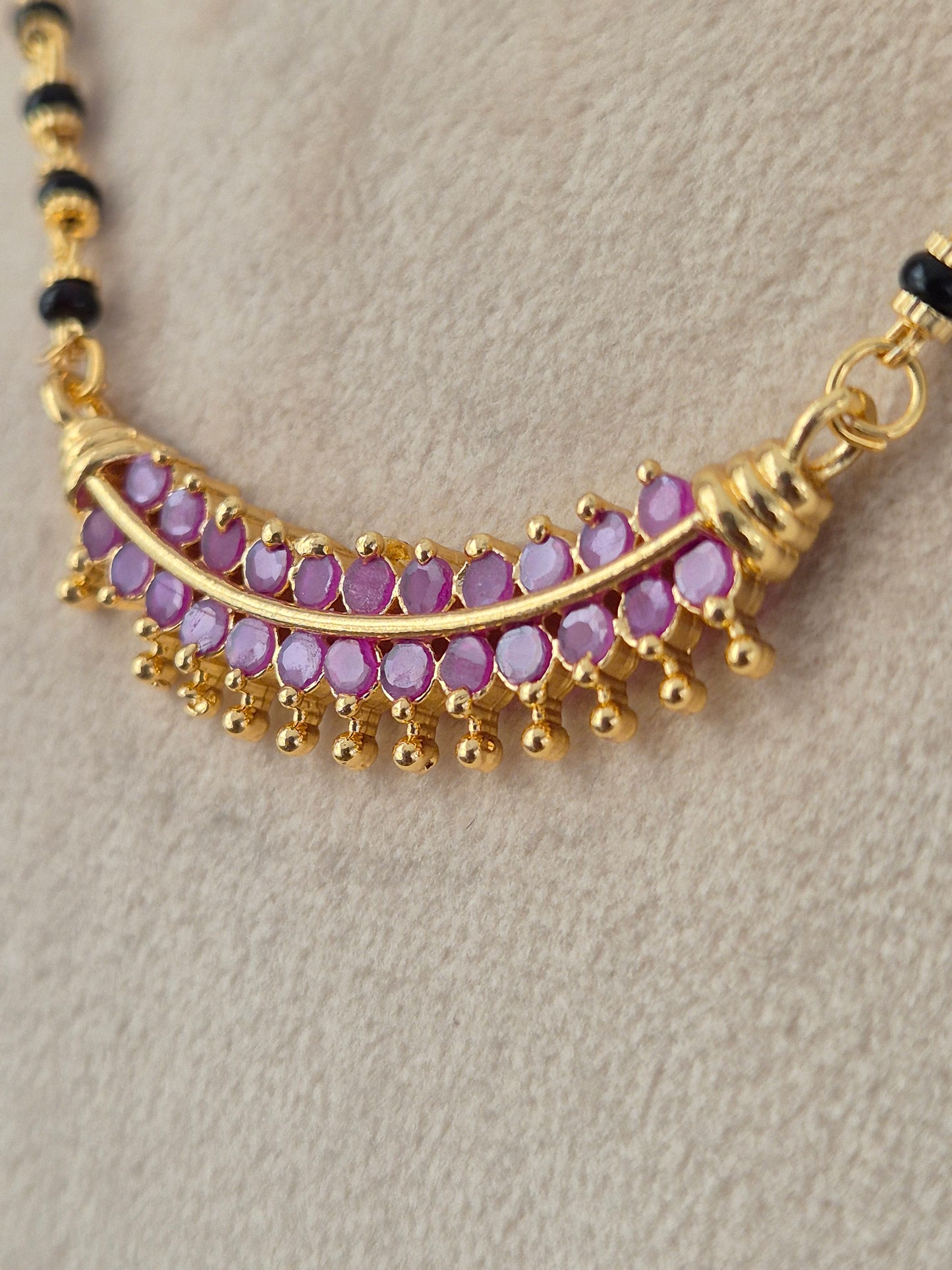 Traditional Indian long mangalsutra set in antique gold finish, featuring a detailed centerpiece pendant with ruby-pink drop stones on a multi-strand black bead chain