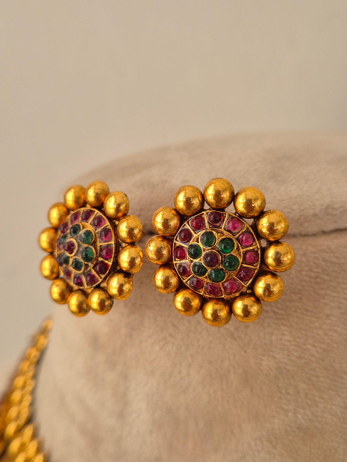Close-up of antique gold circular stud earrings set with red and green stones and surrounded by metallic beads