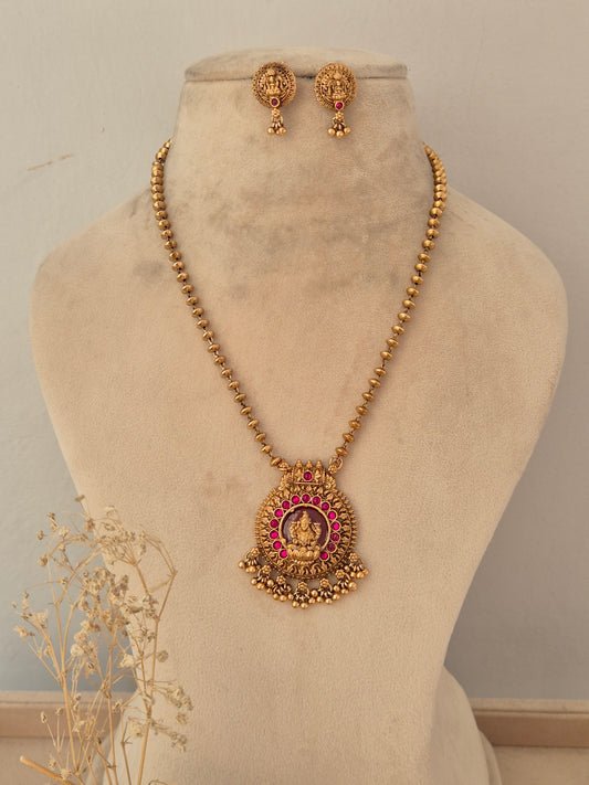Traditional antique gold long necklace set featuring a circular Goddess Laxmi temple pendant with ruby-pink stone embellishments and matching stud earrings