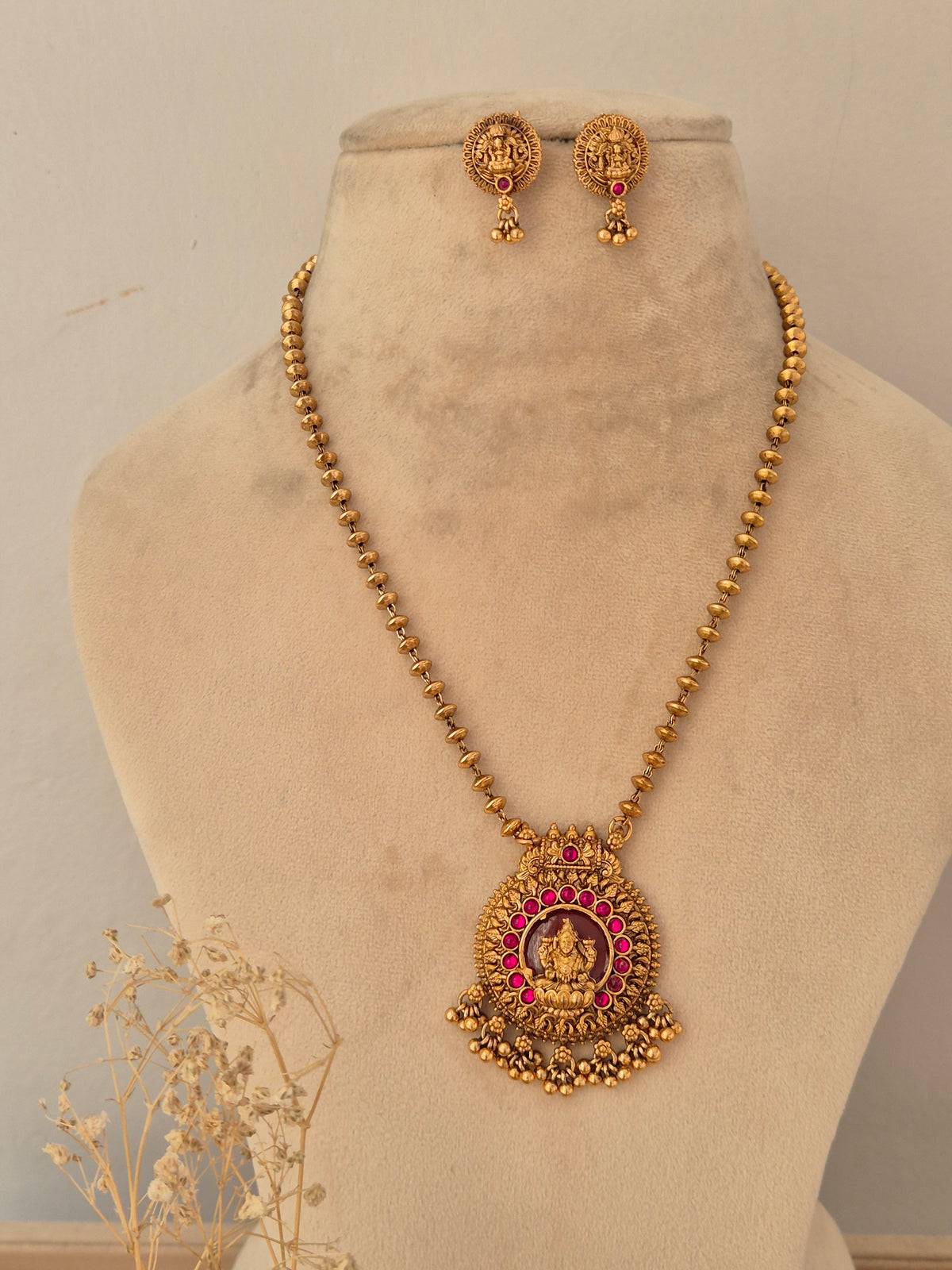 alaja antique gold temple jewellery set showcasing a long beaded chain with a round carved Laxmi pendant framed by a halo of ruby-pink stones, complete with coordinating Goddess motif stud earrings