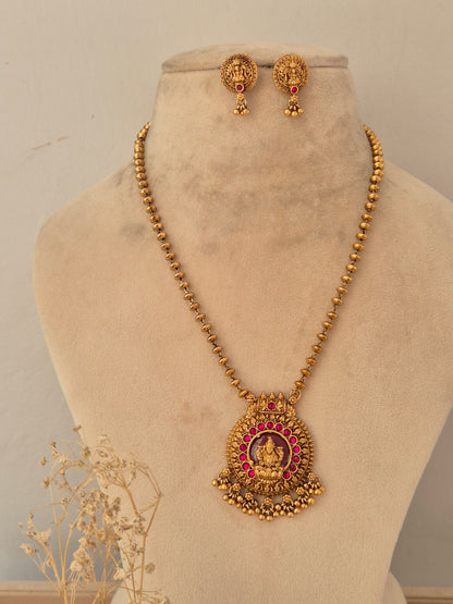 alaja antique gold temple jewellery set showcasing a long beaded chain with a round carved Laxmi pendant framed by a halo of ruby-pink stones, complete with coordinating Goddess motif stud earrings