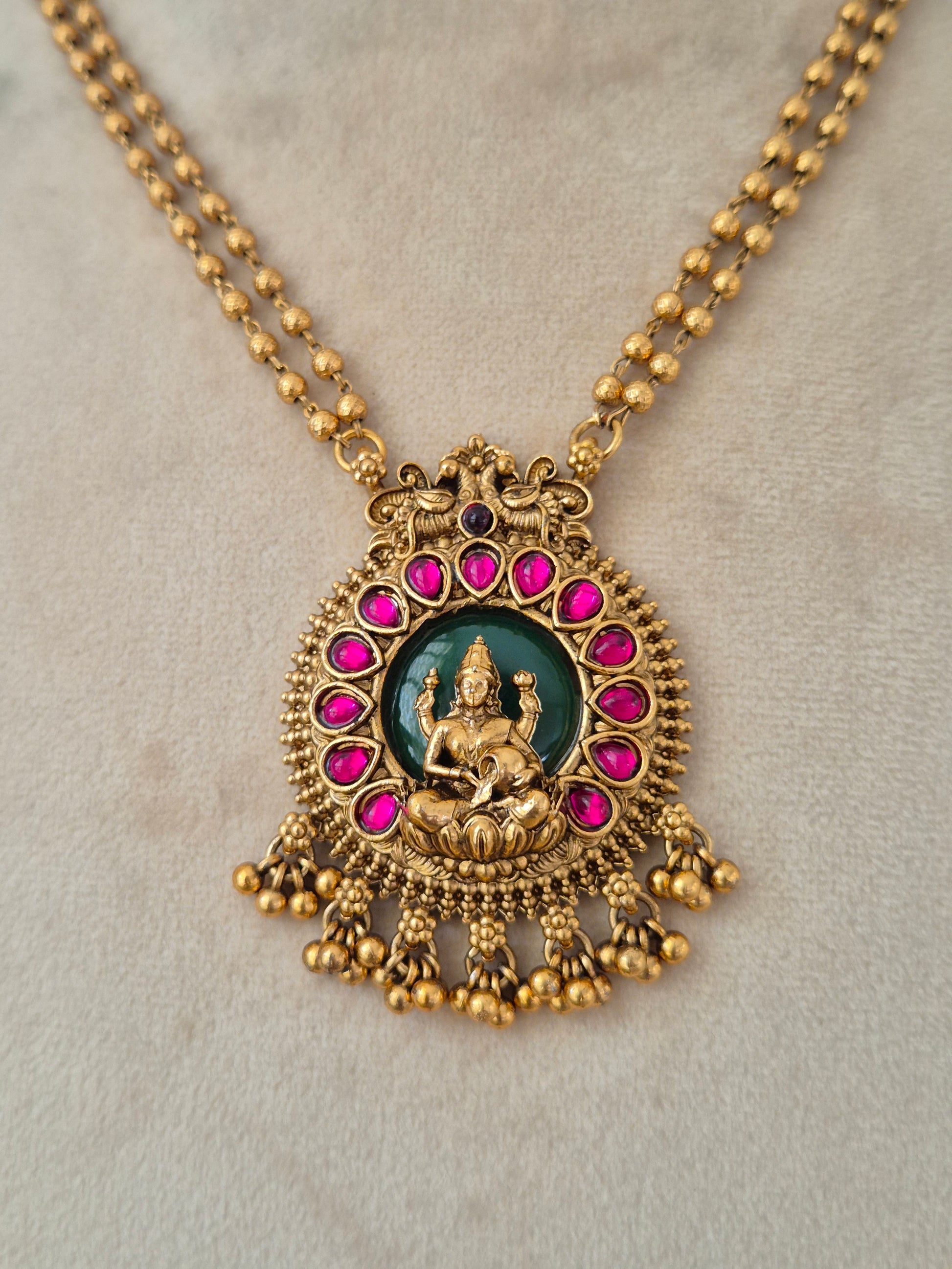 Close-up of an antique gold temple pendant with a Goddess Laxmi motif set against a green background and framed by ruby-pink stones
