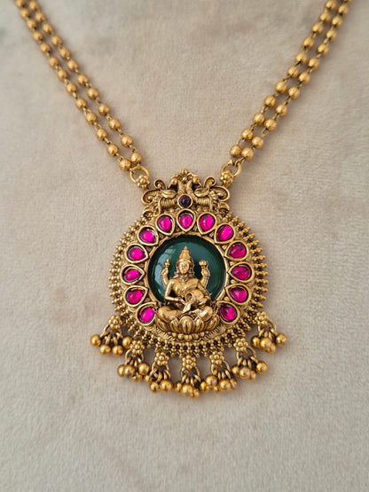 Close-up of an antique gold temple pendant with a Goddess Laxmi motif set against a green background and framed by ruby-pink stones
