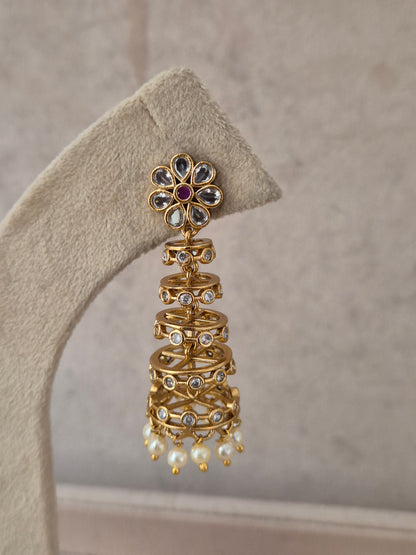 Traditional Indian gold-finish multi-tiered jhumka earring featuring a flower-shaped stud with a central purple-ruby stone, stone-studded wireframe bells, and small pearl bead drops