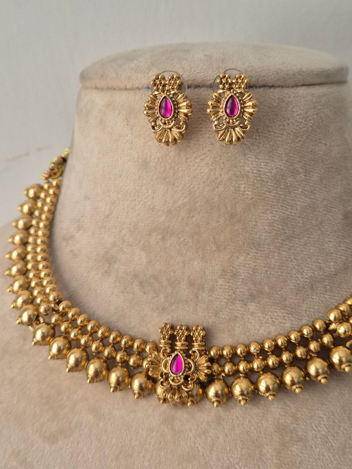 Traditional gold-toned beaded necklace with ruby-pink stone pendant and matching stud earrings