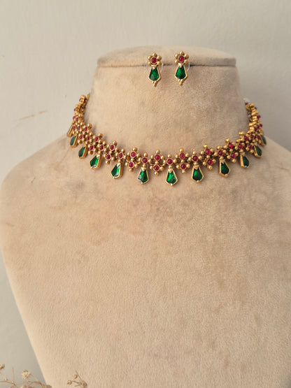 Traditional Indian antique gold choker necklace featuring a row of ruby-red stones embellished with dangling emerald-green teardrop stones, complete with coordinating small drop earrings