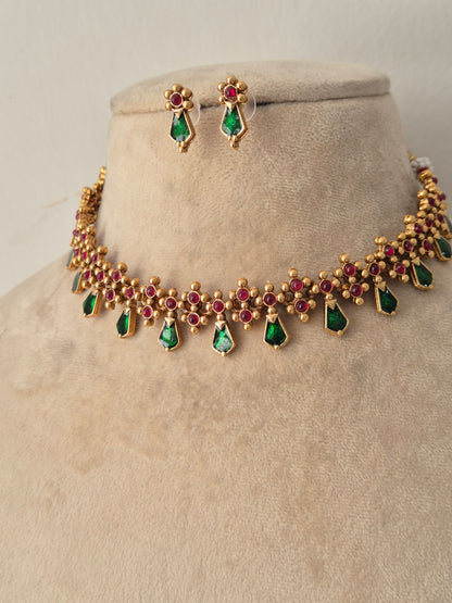 Gold-toned traditional choker with red stone accents, green teardrop dangles, and matching drop earrings on a display bust