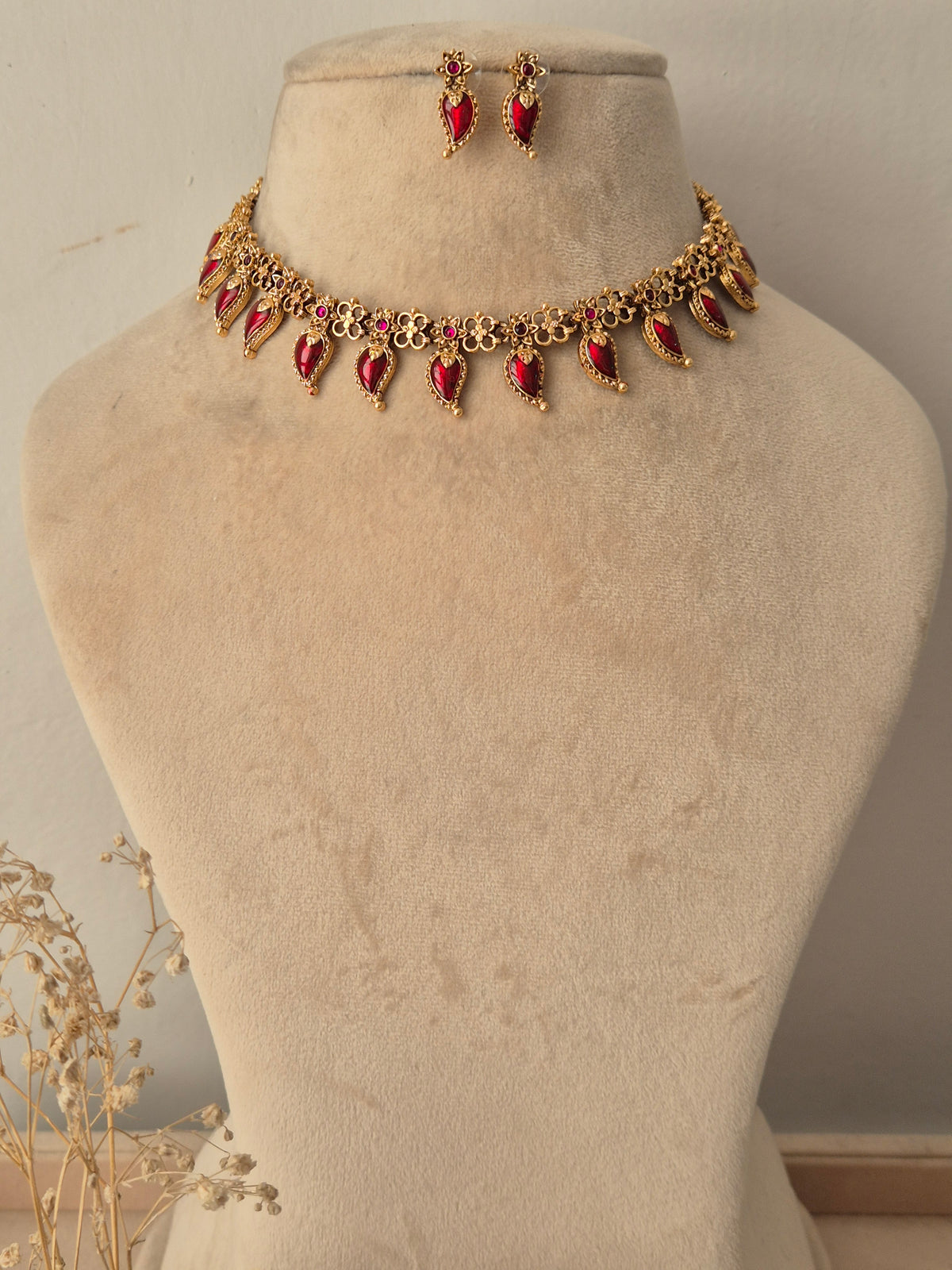 Traditional Indian antique gold choker necklace featuring floral metalwork lined with dangling teardrop-shaped ruby-red stones