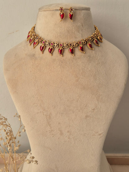 Traditional Indian antique gold choker necklace featuring floral metalwork lined with dangling teardrop-shaped ruby-red stones
