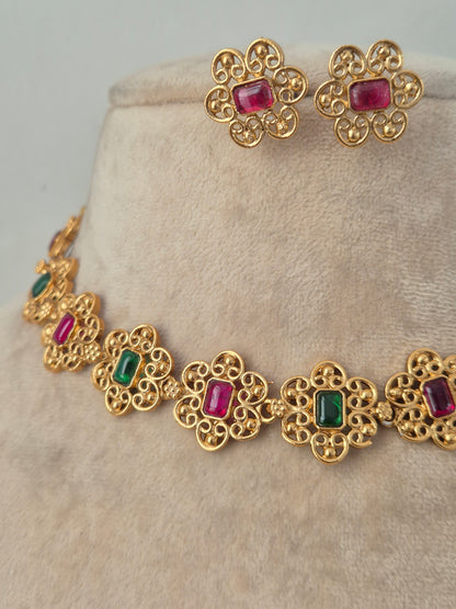 Close-up of an antique gold floral choker necklace set with ruby-red and emerald-green stones, complete with matching floral stud earrings