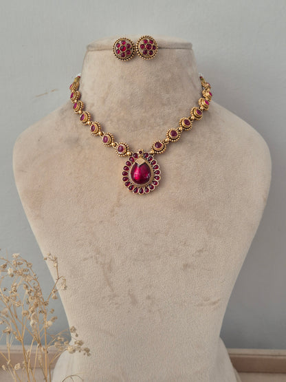 Gold-toned necklace set with a teardrop ruby-pink stone pendant and matching floral stud earrings