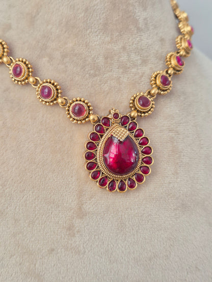 Traditional gold-toned necklace with ruby-pink teardrop pendant and matching stud earrings on a display