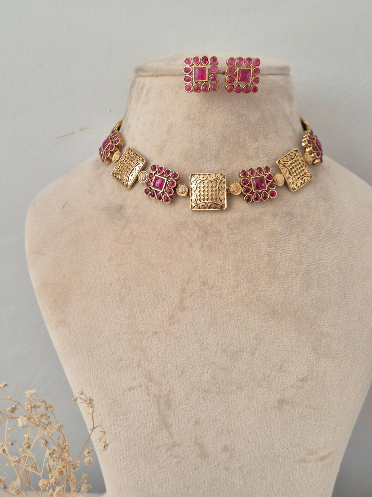 Traditional Indian antique gold choker featuring alternating textured square metal plates and floral motifs studded with ruby-pink gemstones, paired with matching square studs