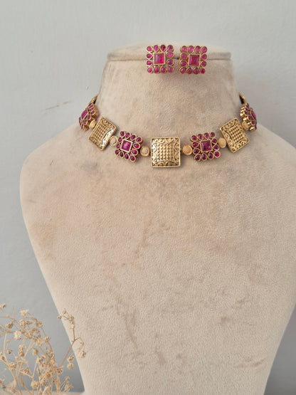 Traditional Indian antique gold choker featuring alternating textured square metal plates and floral motifs studded with ruby-pink gemstones, paired with matching square studs