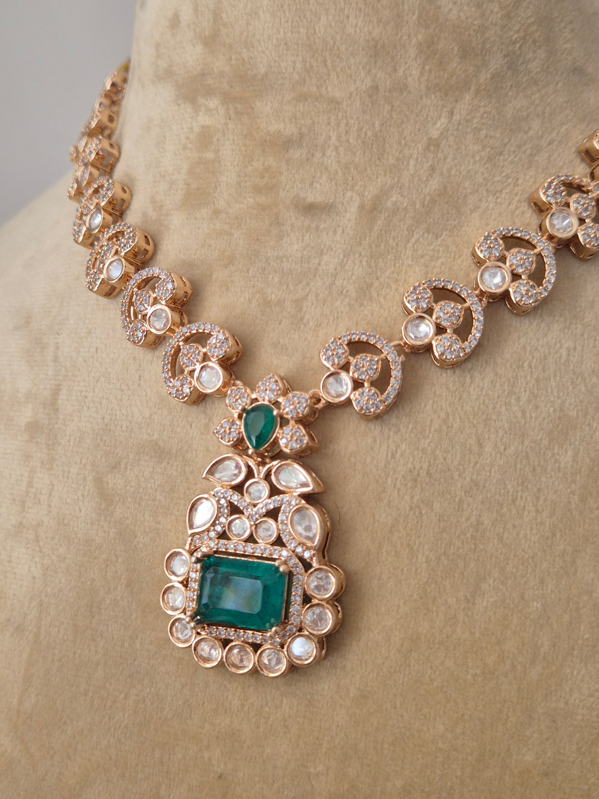 Rose-Gold toned necklace with a large emerald green pendant surrounded by clear crystals by naitri.in