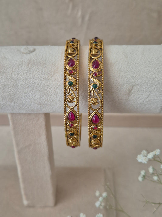 Set of 2 Aadra gold bangles featuring intricate traditional engravings, accented with alternating ruby-red and emerald-green gemstones by naitri.in