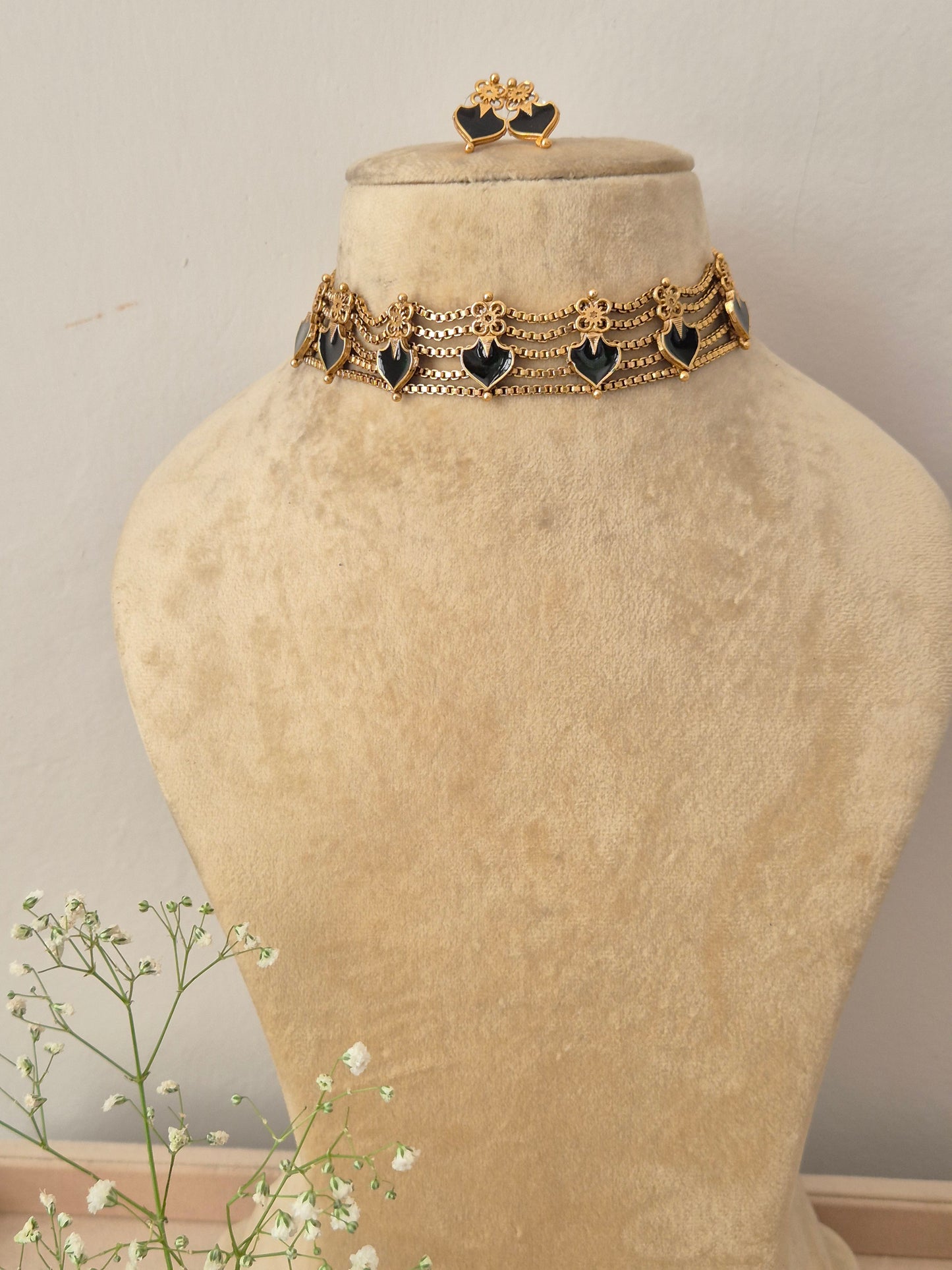 An elegant gold-plated multi-strand choker necklace featuring a repeating pattern of black heart-shaped gemstone charms, with matching heart stud earrings by naitri.in