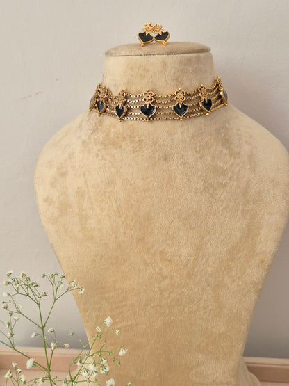 An elegant gold-plated multi-strand choker necklace featuring a repeating pattern of black heart-shaped gemstone charms, with matching heart stud earrings by naitri.in