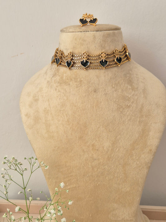 An elegant gold-plated multi-strand choker necklace featuring a repeating pattern of black heart-shaped gemstone charms, with matching heart stud earrings by naitri.in