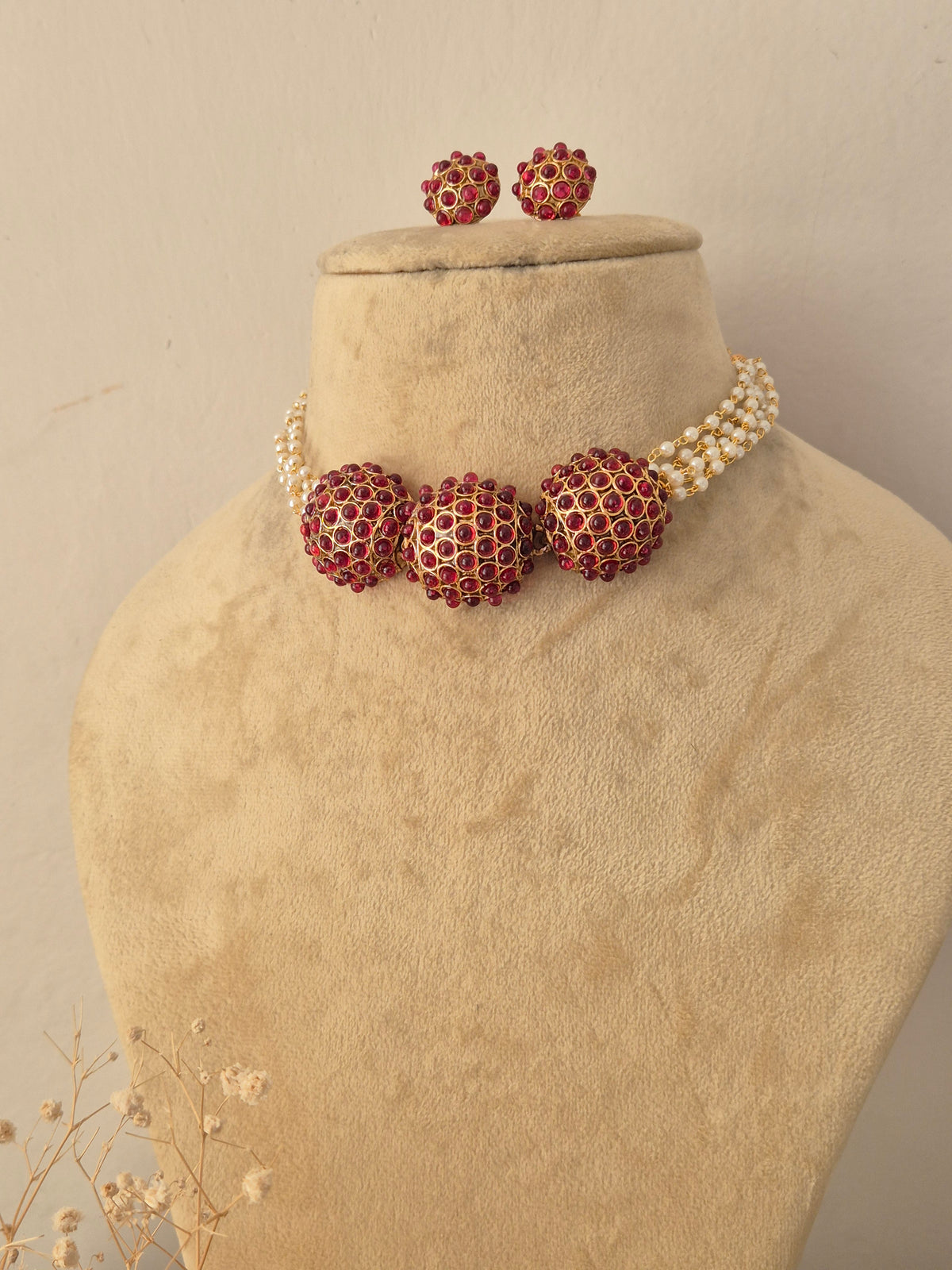 Traditional Indian gold-toned choker necklace with red stone-studded round centerpieces and pearl strands, accompanied by matching red stone stud earrings by Naitri.in