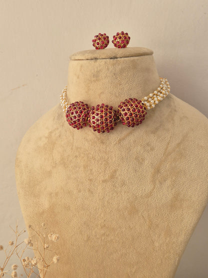 Traditional Indian gold-toned choker necklace with red stone-studded round centerpieces and pearl strands, accompanied by matching red stone stud earrings by Naitri.in