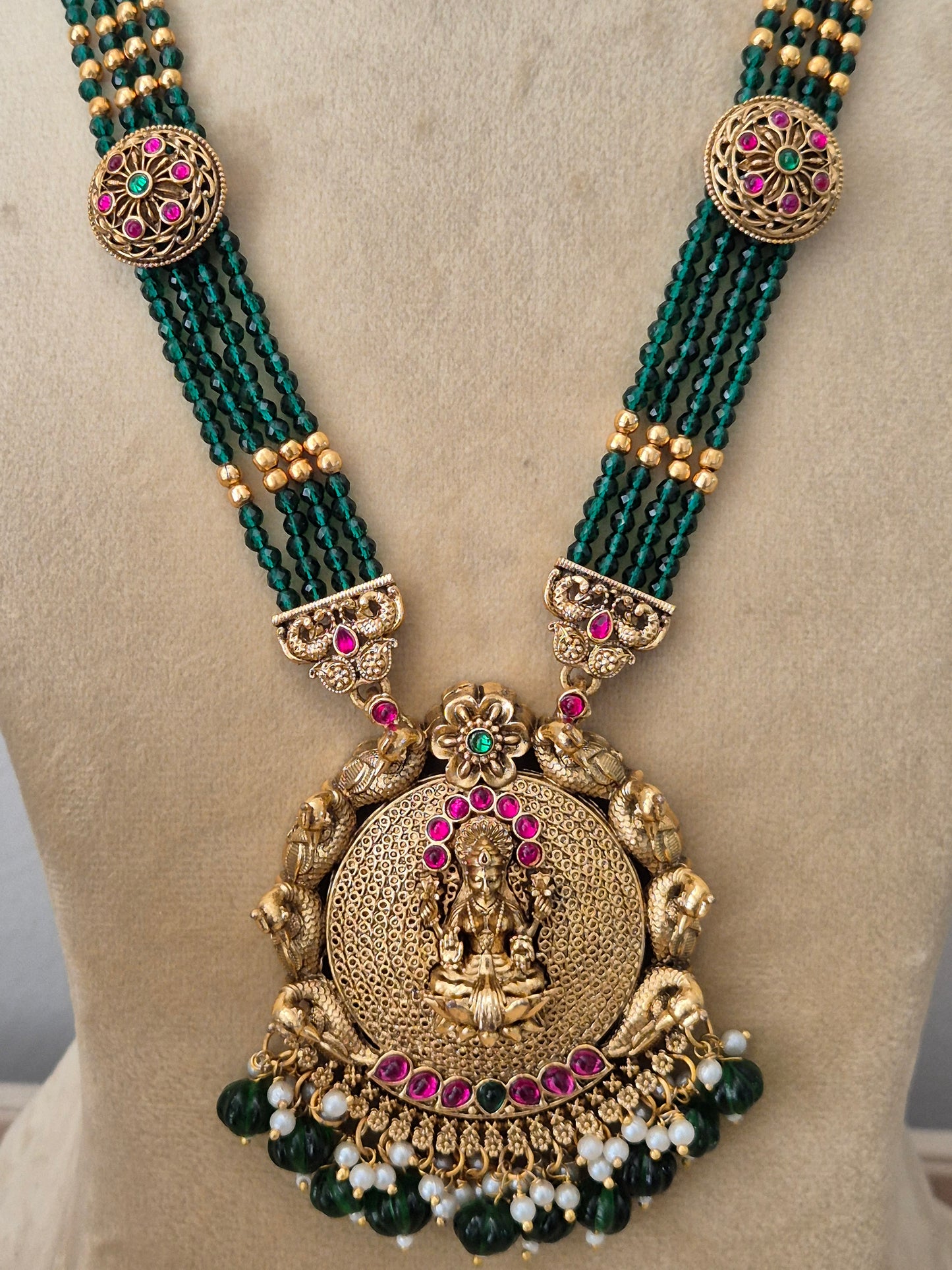 Traditional Indian ethnic imitation jewelry set featuring a layered emerald-green beaded strand necklace, a detailed gold temple pendant, and matching hanging earrings with tiny white pearl drops by naitri.in
