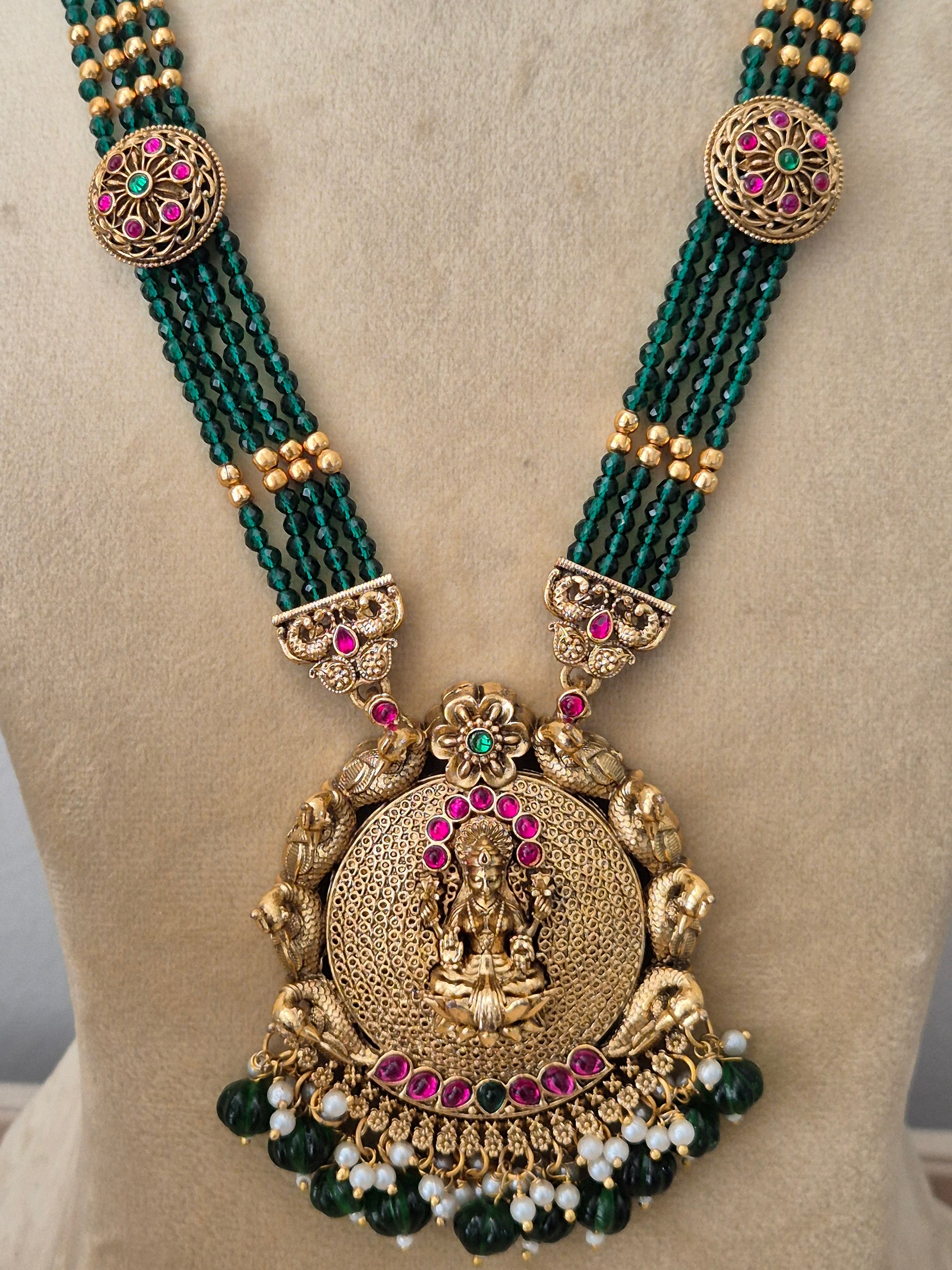 Traditional Indian ethnic imitation jewelry set featuring a layered emerald-green beaded strand necklace, a detailed gold temple pendant, and matching hanging earrings with tiny white pearl drops by naitri.in