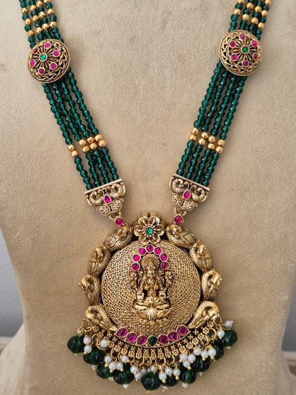 Traditional Indian ethnic imitation jewelry set featuring a layered emerald-green beaded strand necklace, a detailed gold temple pendant, and matching hanging earrings with tiny white pearl drops by naitri.in