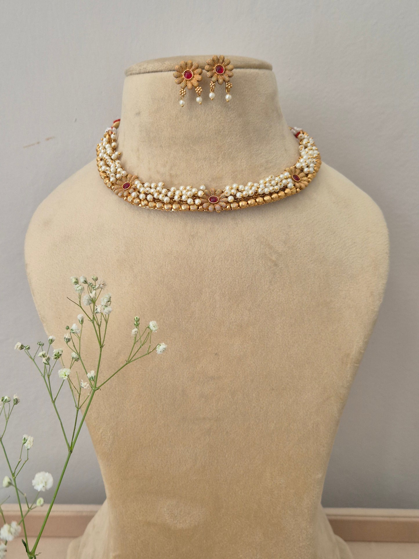 Elegant gold necklace set featuring multiple strands of white pearls and a central red stone floral pendant, with matching earrings by naitri.in