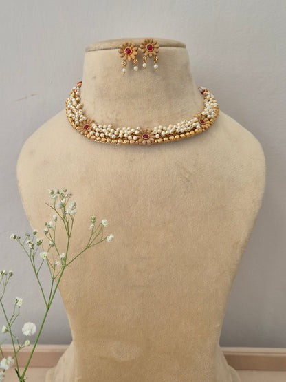 Elegant gold necklace set featuring multiple strands of white pearls and a central red stone floral pendant, with matching earrings by naitri.in