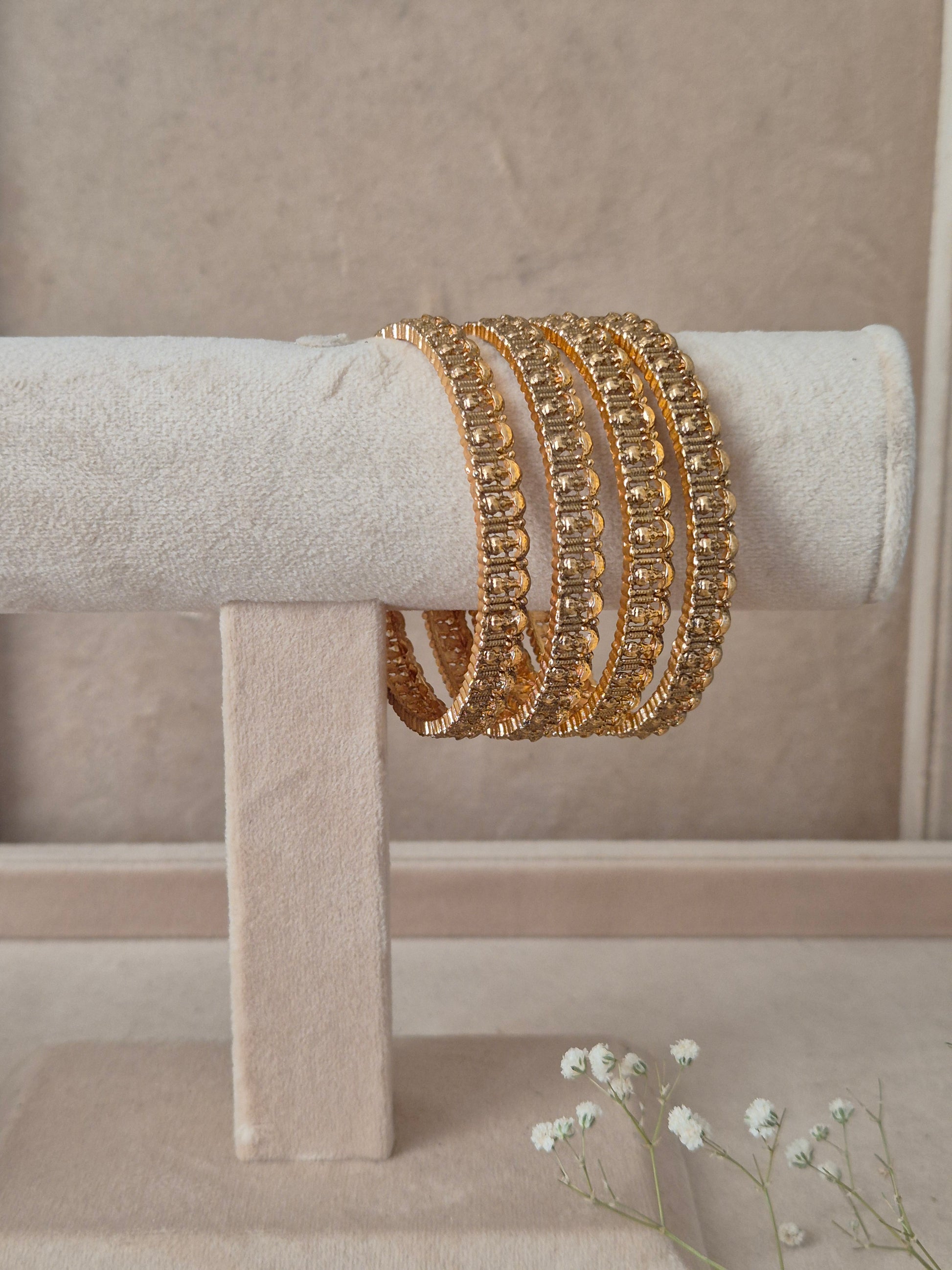 A stack of four Naitri Aaravi gold bangles showcasing detailed traditional craftsmanship and reflective textures by naitri.in