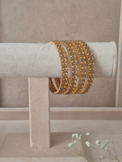 A stack of four Naitri Aaravi gold bangles showcasing detailed traditional craftsmanship and reflective textures by naitri.in