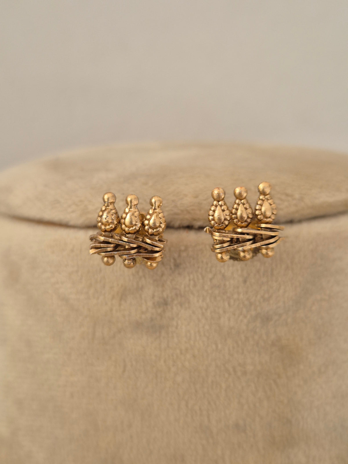 Pair of gold-toned textured stud earrings with crown-like top motifs by naitri.in