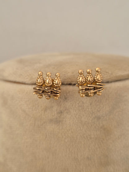 Pair of gold-toned textured stud earrings with crown-like top motifs by naitri.in