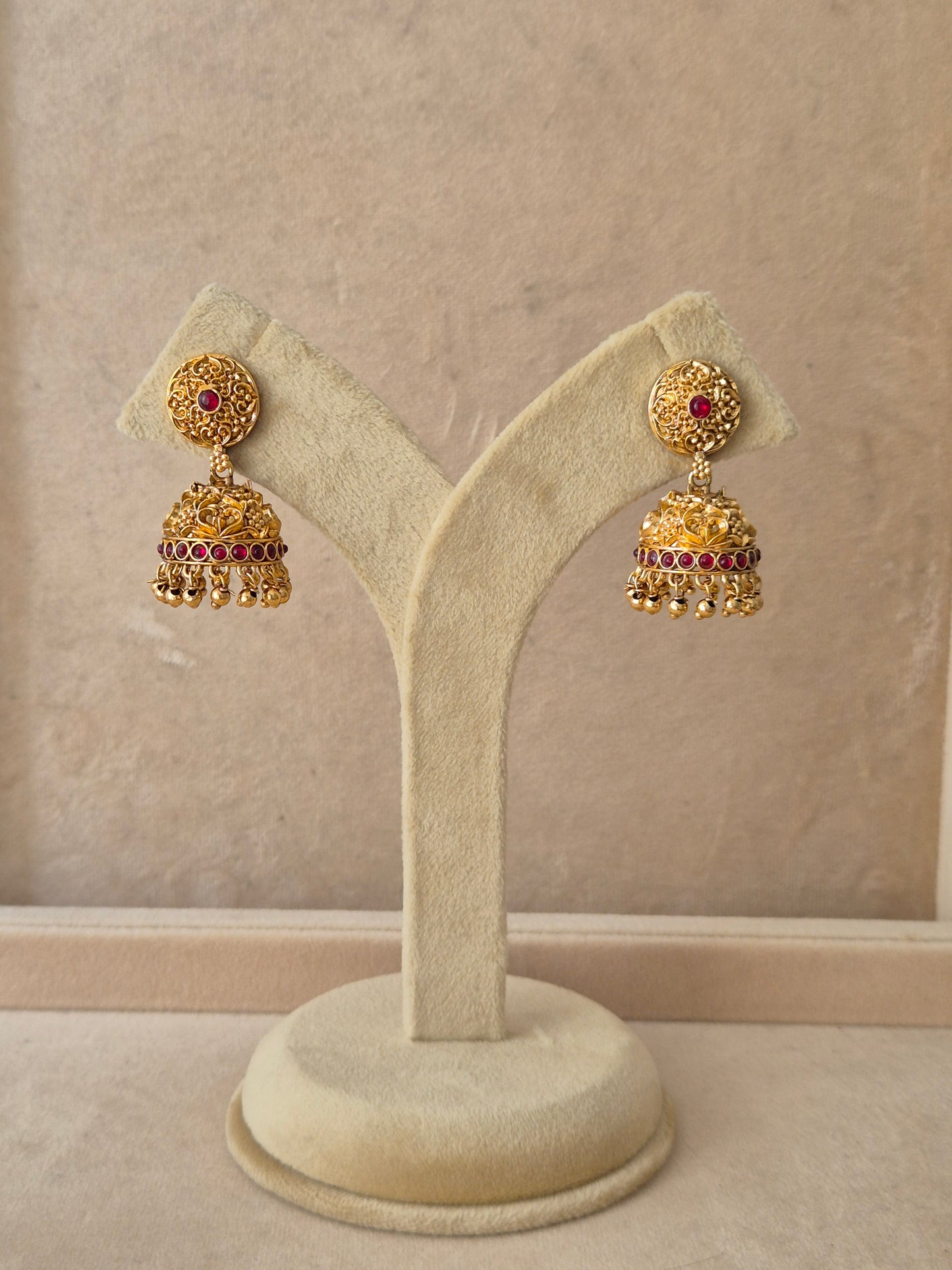 Pair of gold-plated Jhumki earrings featuring intricate metalwork, red stone accents, and delicate hanging bead drops by naitri.in
