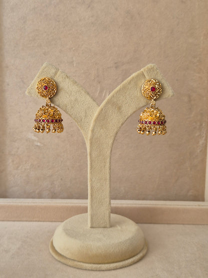 Pair of gold-plated Jhumki earrings featuring intricate metalwork, red stone accents, and delicate hanging bead drops by naitri.in