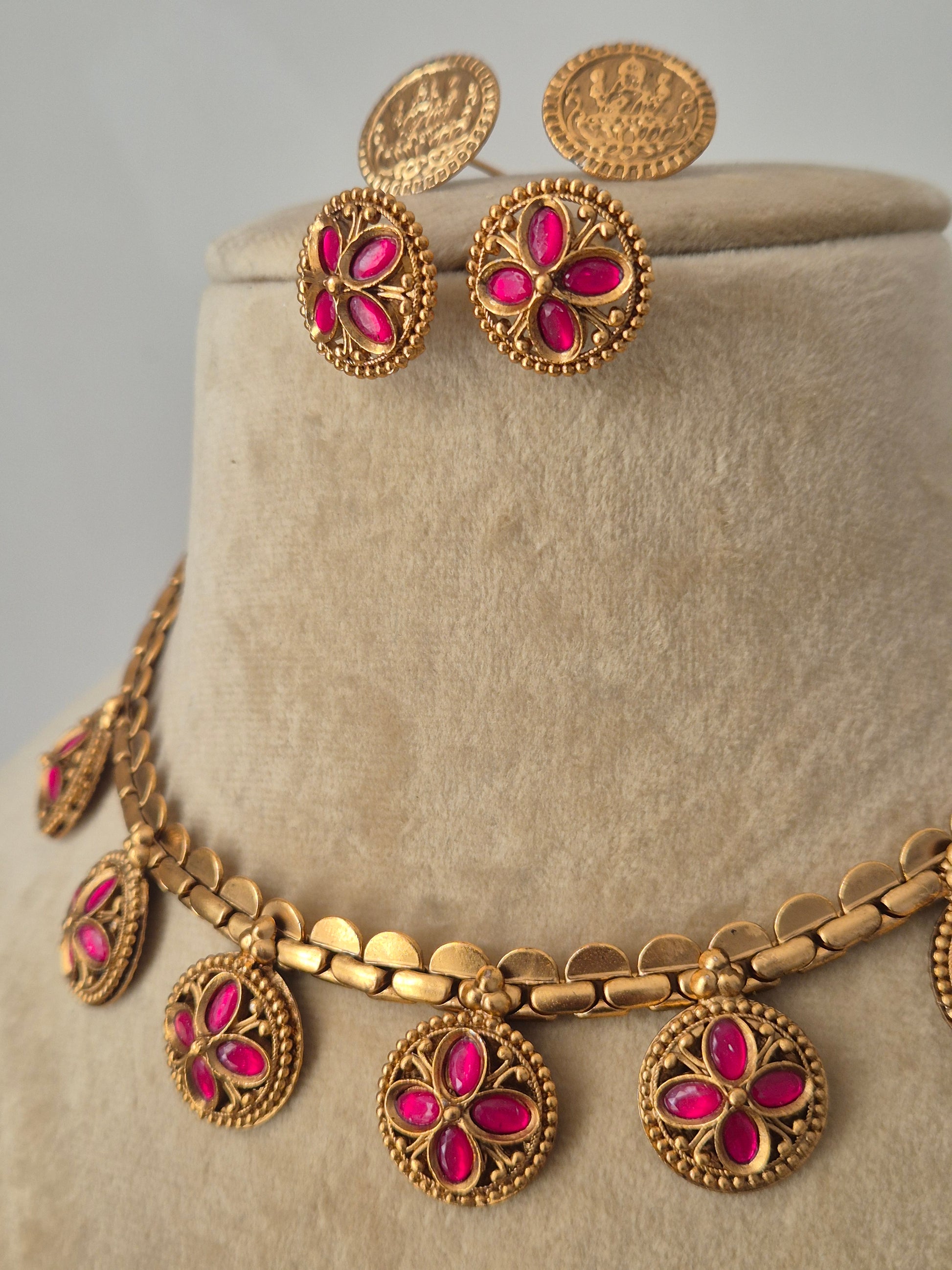 Elegant golden choker necklace with circular links and ruby-pink stone floral charms, displayed on a mannequin with coordinating earrings by naitri.in