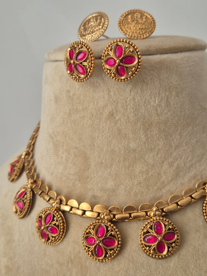 Elegant golden choker necklace with circular links and ruby-pink stone floral charms, displayed on a mannequin with coordinating earrings by naitri.in