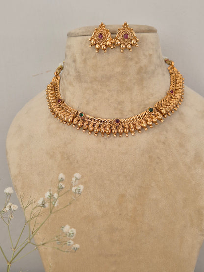 Gold-polished textured ethnic choker with red and green stone embellishments, dangling gold beads, and coordinating festive earrings by naitri.in