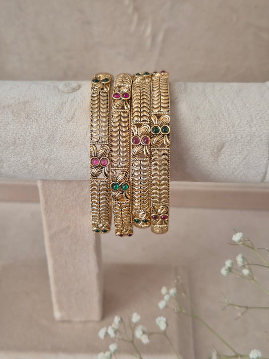 Set of 4 Ahilya gold bangles by Naitri featuring intricate traditional engravings, accented with alternating ruby-red and emerald-green gemstones, by naitri.in