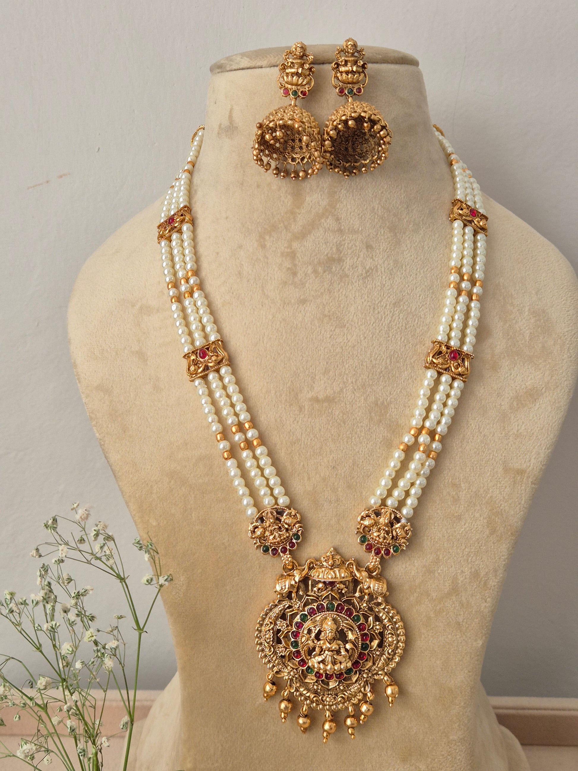 Traditional multi-strand pearl necklace with a large antique gold deity pendant and matching jhumka earrings, by naitri.in