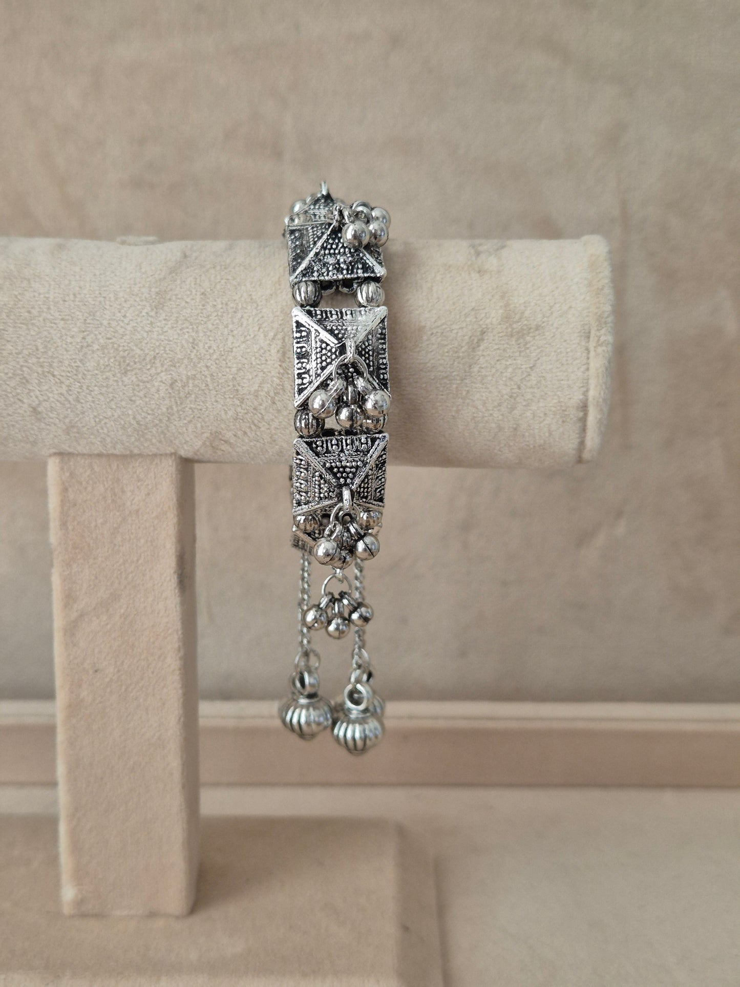 Oxidized silver Alaknanda bangle bracelet with intricate geometric patterns, textured pyramid elements, and dangling ghungroo metallic beads by naitri.in